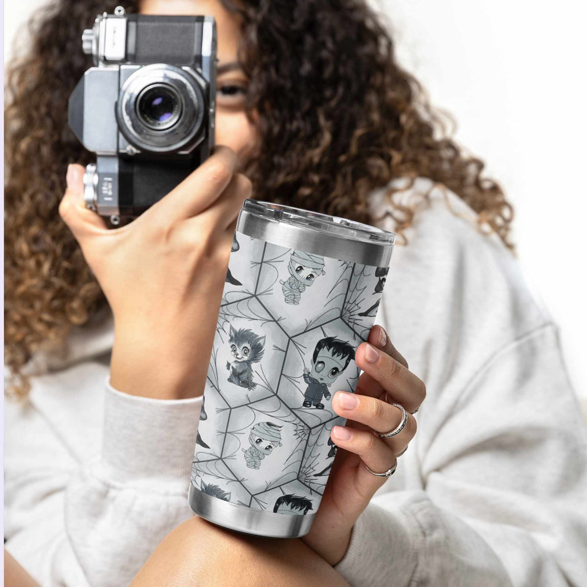 Woman in a white sweatshirt holding a vintage camera and the black and white monster tumbler