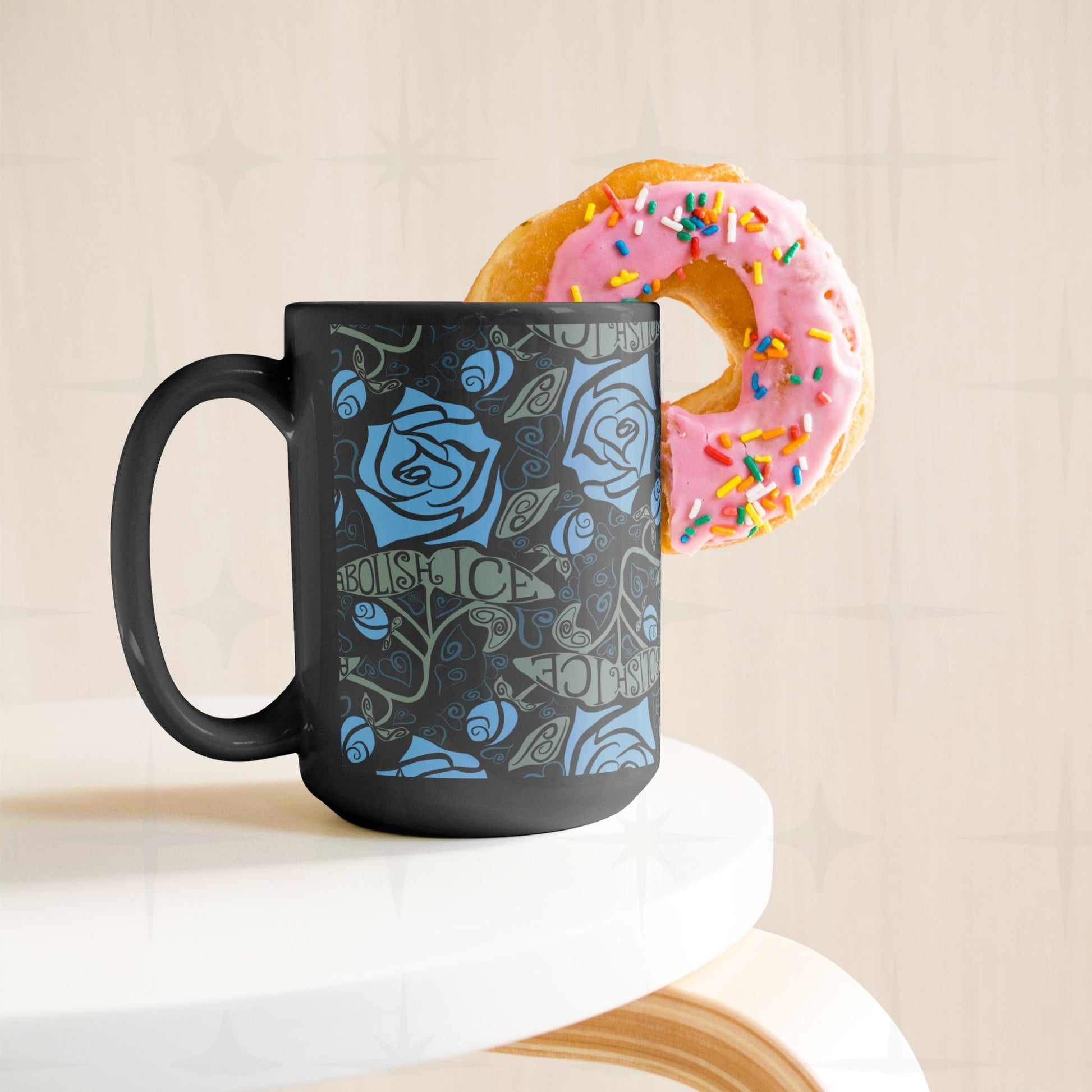 Abolish ICE coffee mug on white surface styled with a pink sprinkle donut, black ceramic gothic rose wrap print
