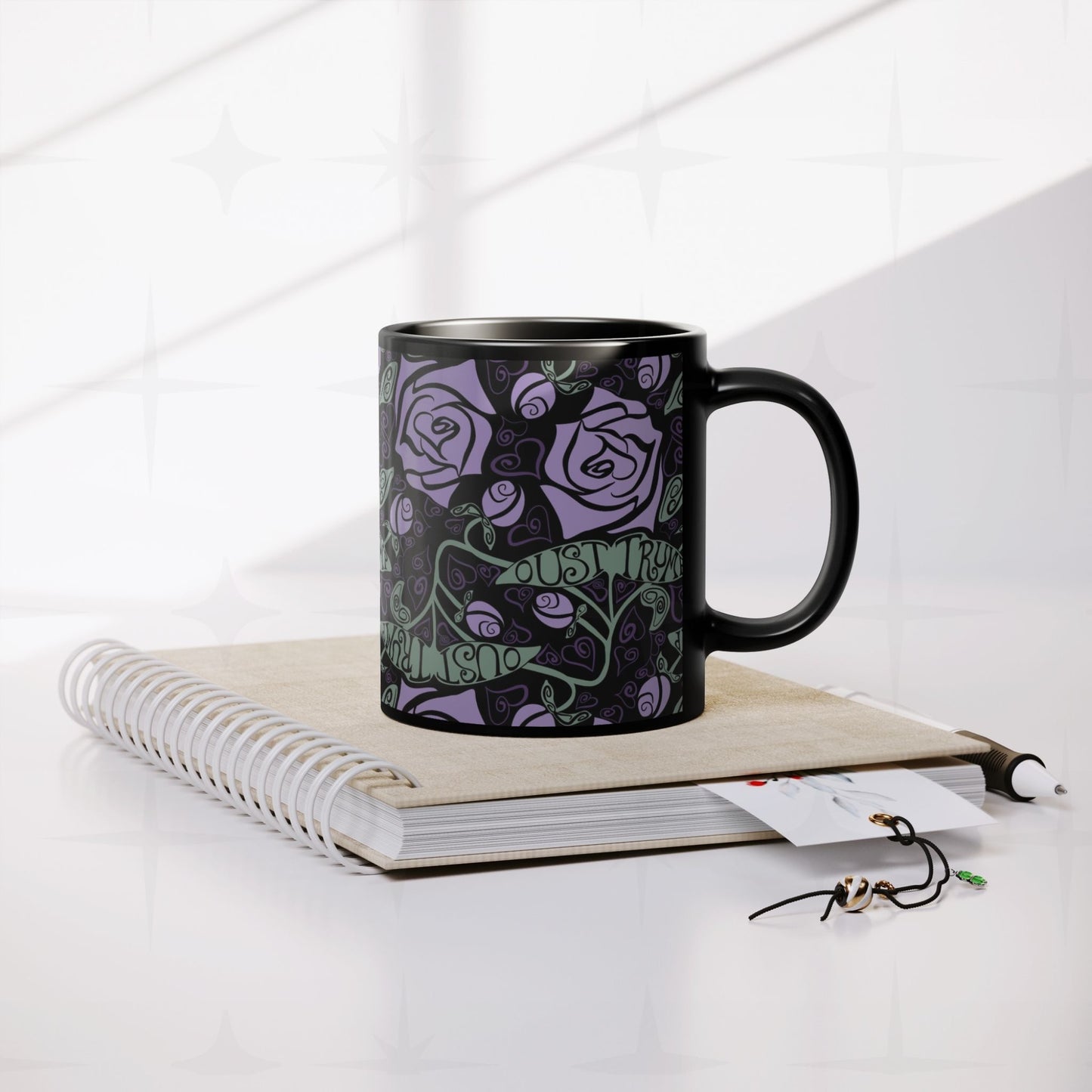 Anti-Trump hidden message black ceramic mug resting on spiral notebook with pen and accessories