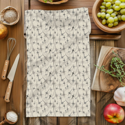 Overhead flat lay of a gray mid century modern tea towel on a rustic wood surface surrounded by kitchen props including a whisk, knife, grapes, apple, garlic, and fresh herbs