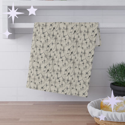 Warm gray atomic starburst cotton twill kitchen towel hanging from a round chrome hook against bright white subway tile with wooden shelves and stacked plates visible