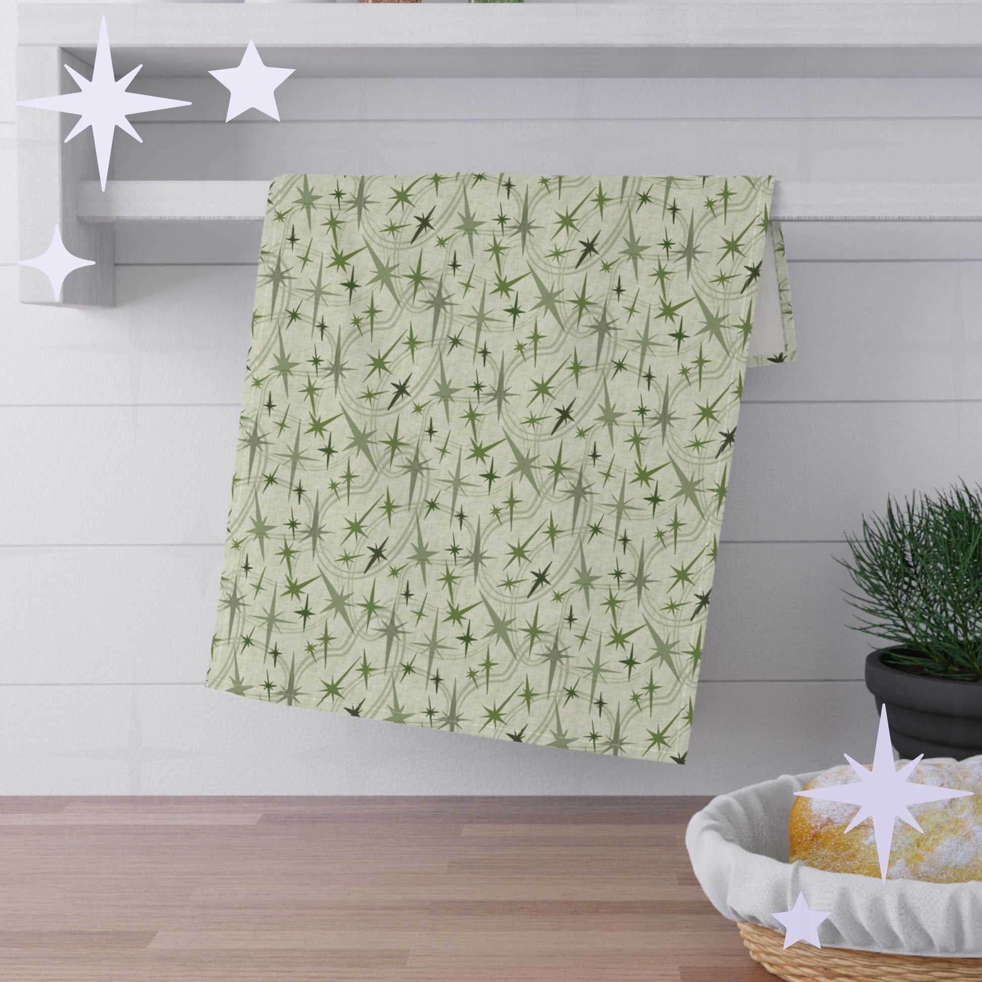 Sage green atomic starburst kitchen towel hanging from while towel bar against bright white subway tile over a wooden countertop