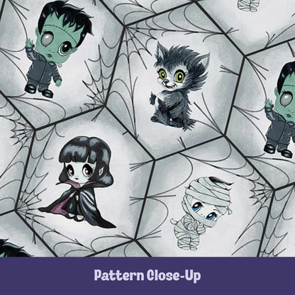 Close-up of the chibi monster pattern showing mint green Frankenstein, chartreuse-eyed werewolf, plum-lined vampire cape, and blue-eyed mummy on a charcoal spiderweb lattice
