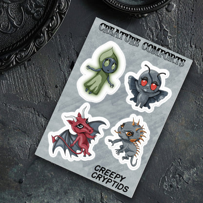 Cryptid sticker sheet on a slate surface next to a scrolled black metal frame