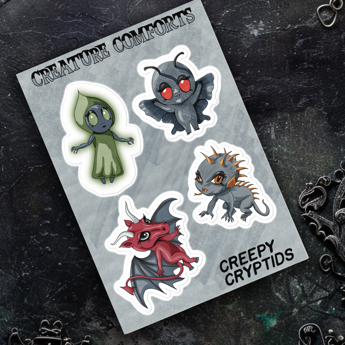 Creepy Cryptids sticker sheet resting on dark textured stone beside ornate silver filigree jewelry