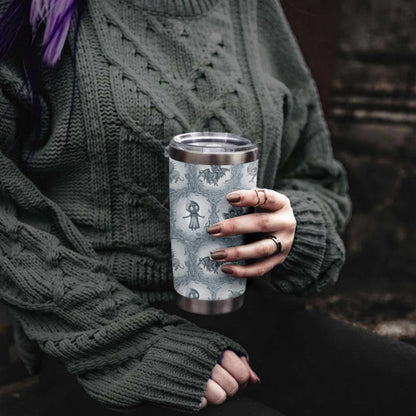 Woman with purple hair in a green cable-knit sweater holding the cool gray cryptid tumbler in a stone doorway