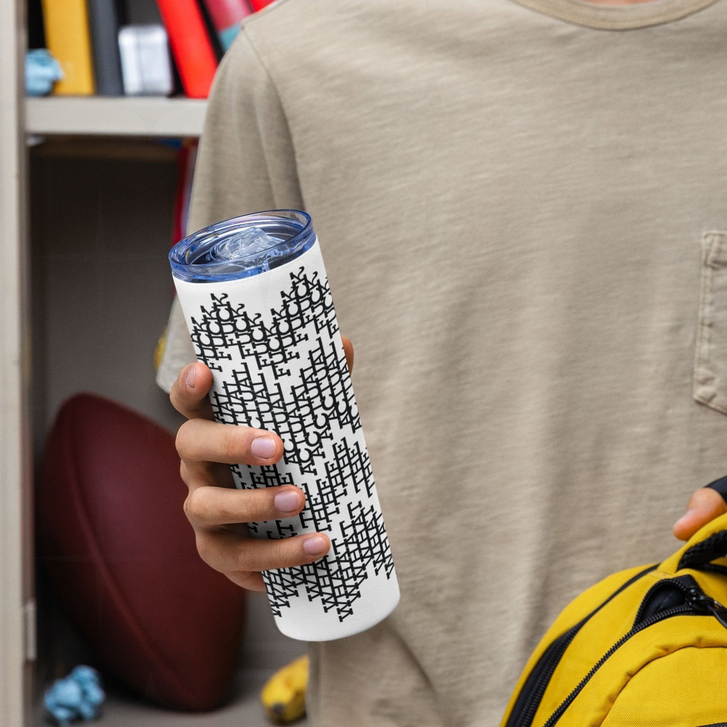 Person holding the black stripes sarcastic tumbler near a locker with a yellow backpack, showing the all-over hidden message typographic pattern
