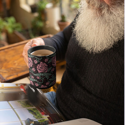 Person reading a magazine with the Fight Fascism black ceramic mug on a table, Art Nouveau floral wrap print visible