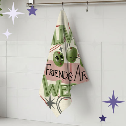 Retro illustrated olive tea towel hanging from a wall hook in a white tiled kitchen, showing "... Friends Are Weird" lettering