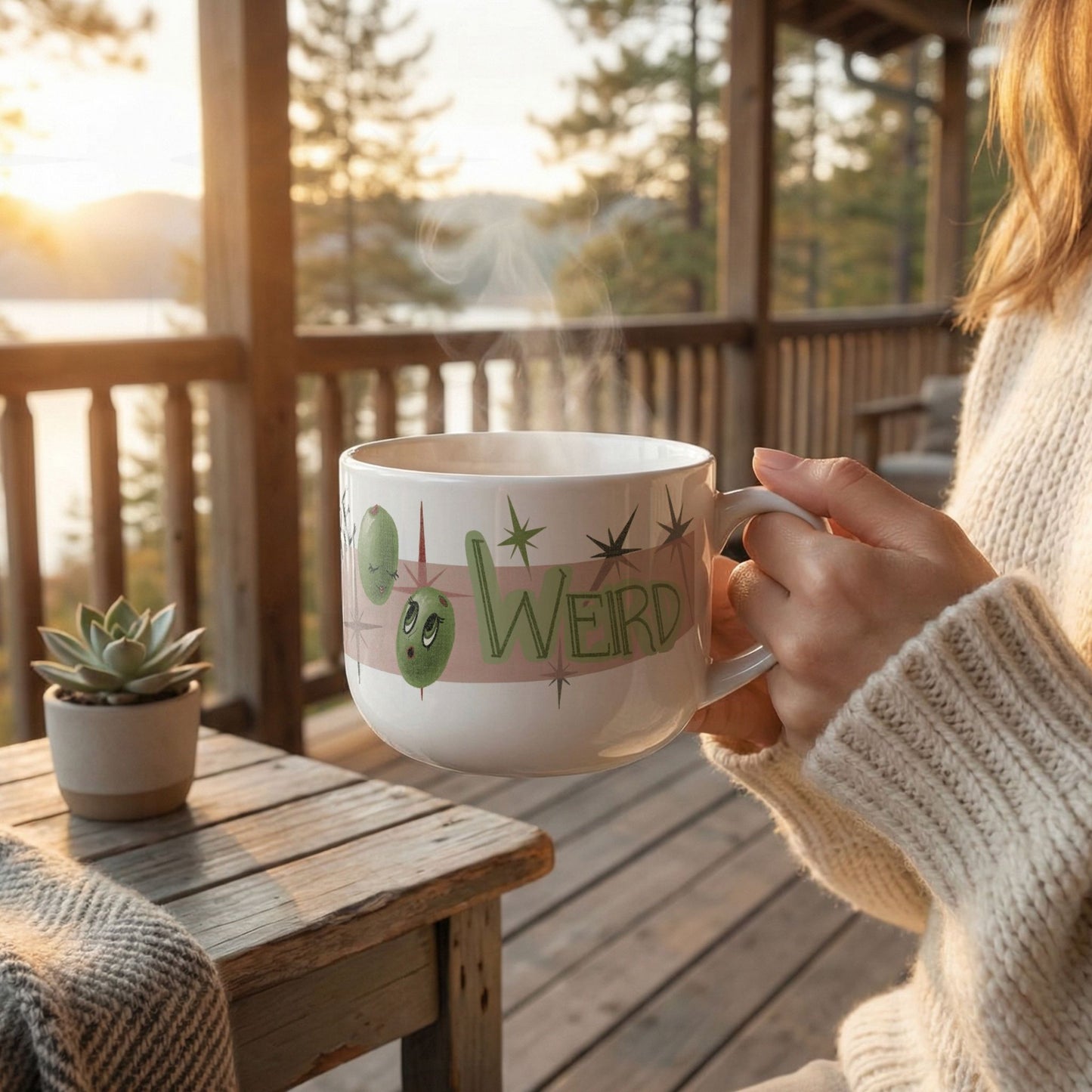Woman in cream knit sweater holding 25oz funny mom mug with steam rising on a rustic cabin porch at golden hour, retro Olive My Kids Are Weird olive pun design facing forward