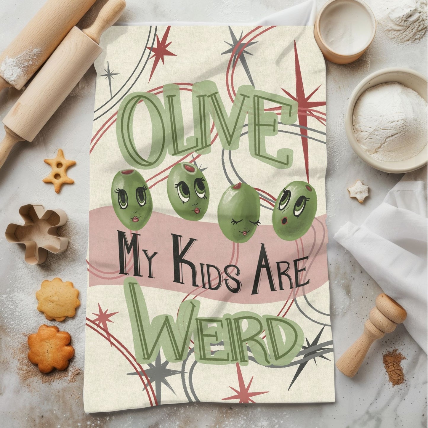 Funny olive pun kitchen tea towel on marble surface with baking props, retro mid-century illustration with sage green lettering and atomic starburst design