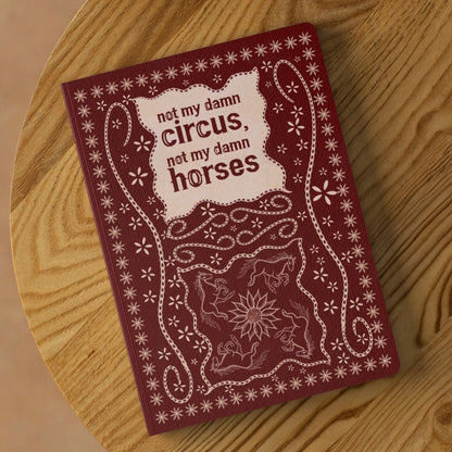 Not my circus folk art lined journal on round wooden table showing burgundy softcover with stitched horse and sunflower illustration