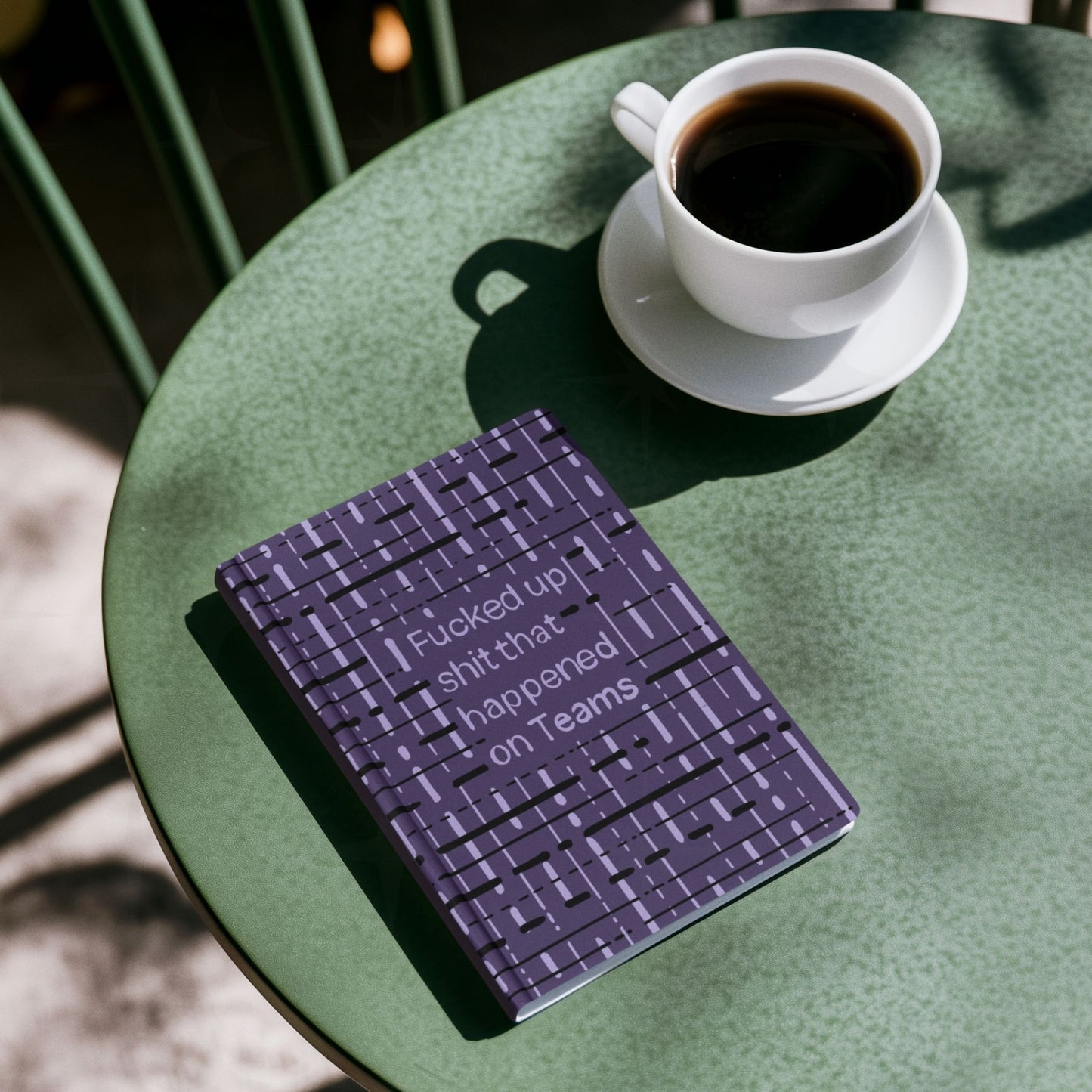 Funny Teams profanity hardcover journal on green café table next to cup of black coffee
