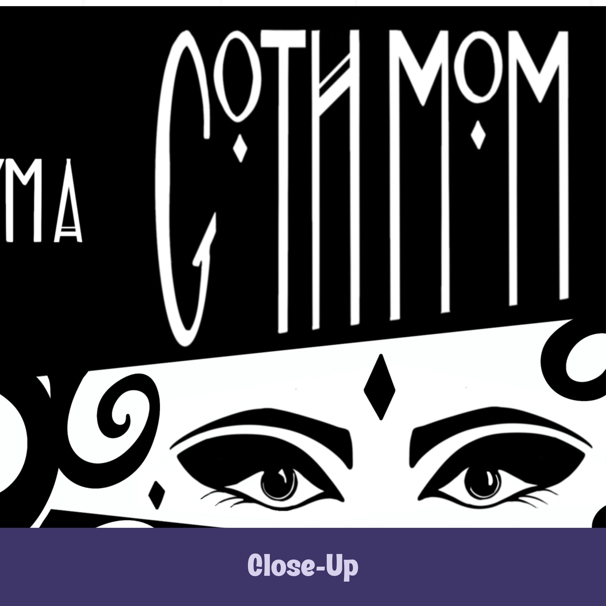 Close-up of gothic coffee mug showing Goth Mom lettering above hand-drawn masquerade-style eyes with winged liner and diamond gem on white band on black ceramic