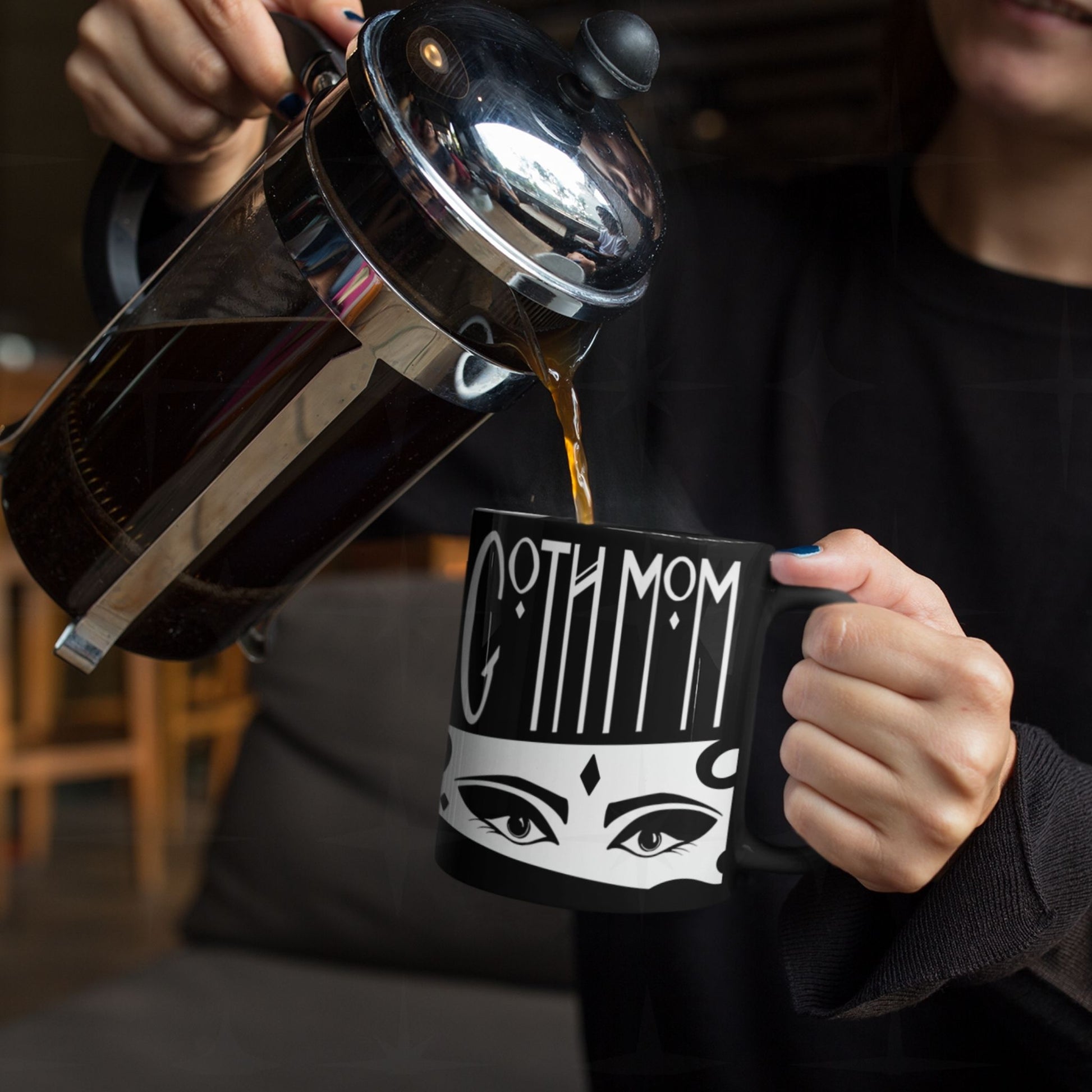 Coffee being poured from French press into black Goth Mom ceramic mug with gothic Art Deco hand lettering and illustrated eyes, lifestyle shot