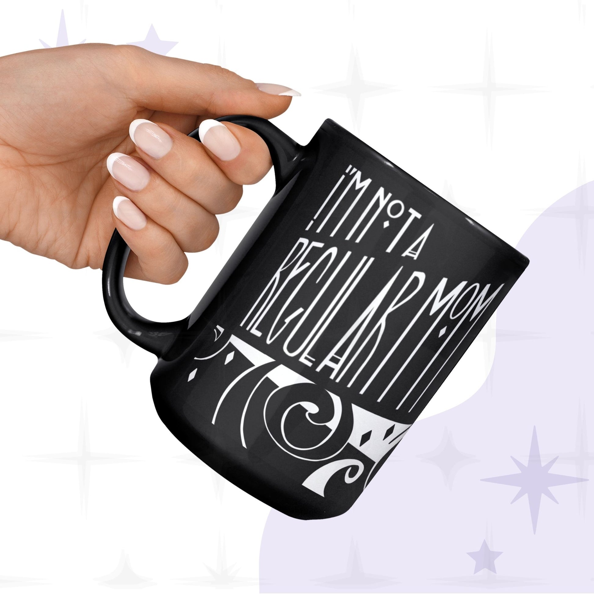 Hand holding black goth mom coffee mug from below showing I'm Not a Regular Mom gothic lettering and baroque scroll illustration, glossy ceramic