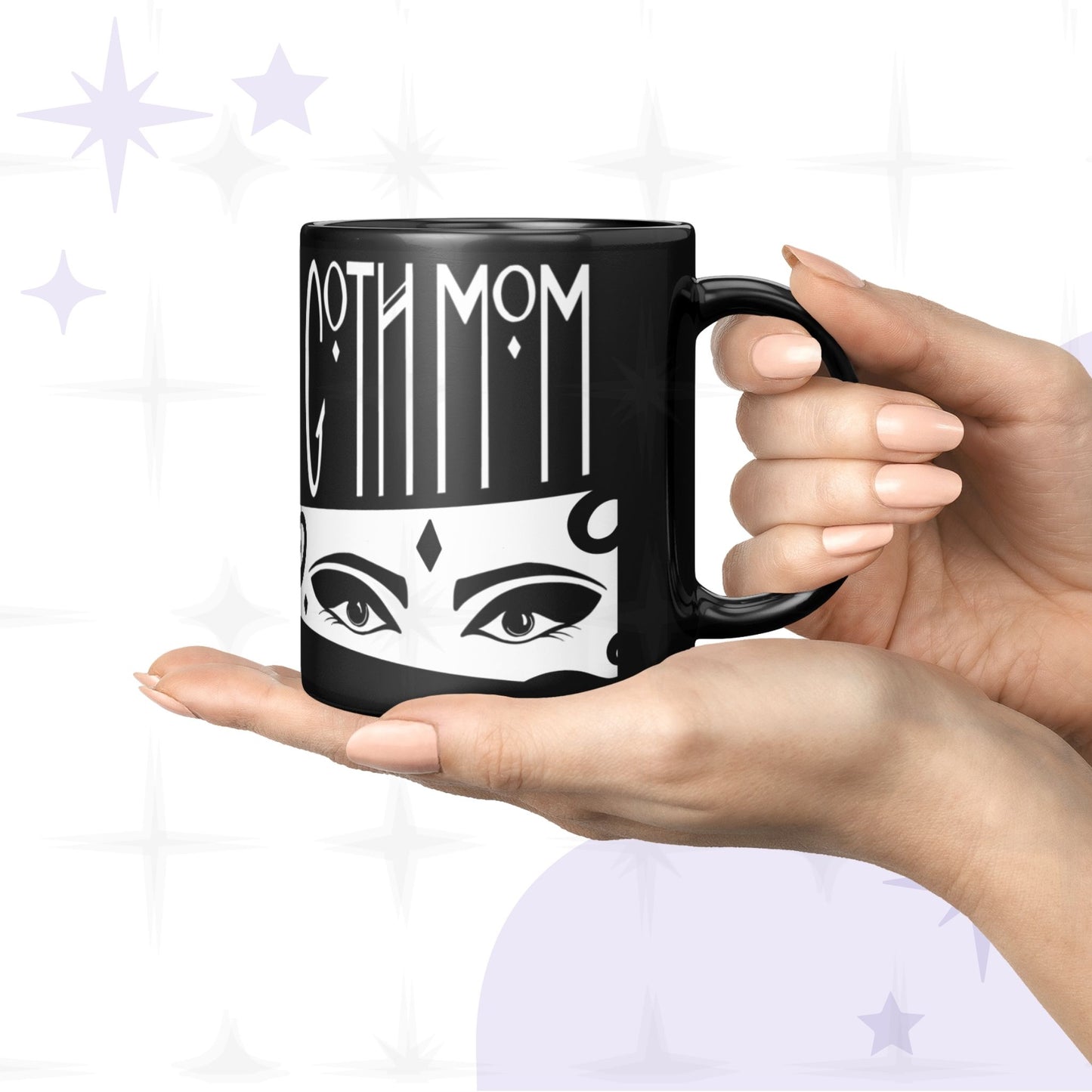Two hands cradling small 11oz black goth mom mug with Goth Mom gothic lettering and illustrated eyes with winged liner, white background