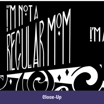 Close-up of goth mom mug showing hand-lettered I'm Not a Regular Mom in tall gothic Art Deco type with diamond accents and baroque scroll illustration on black ceramic