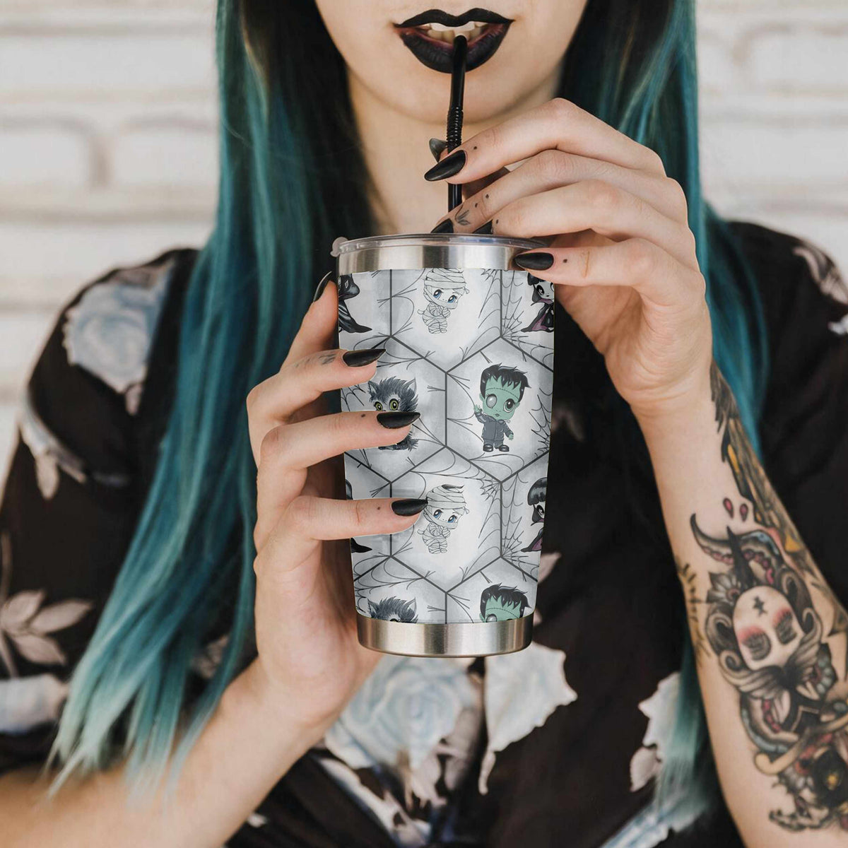 Woman with teal hair, black lipstick, and tattoos drinking from the chibi monster goth tumbler through a black straw
