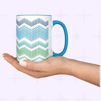 Lifestyle shot of a hand holding the Ocean Blue 15oz hidden message mug from below, showing the full-wrap chevron pattern against a soft lavender background