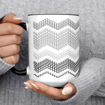 Lifestyle close-up of two hands in a gray cable-knit sweater holding the Gray and Black 15oz hidden message mug, with the hidden stitch text partially visible in the second band