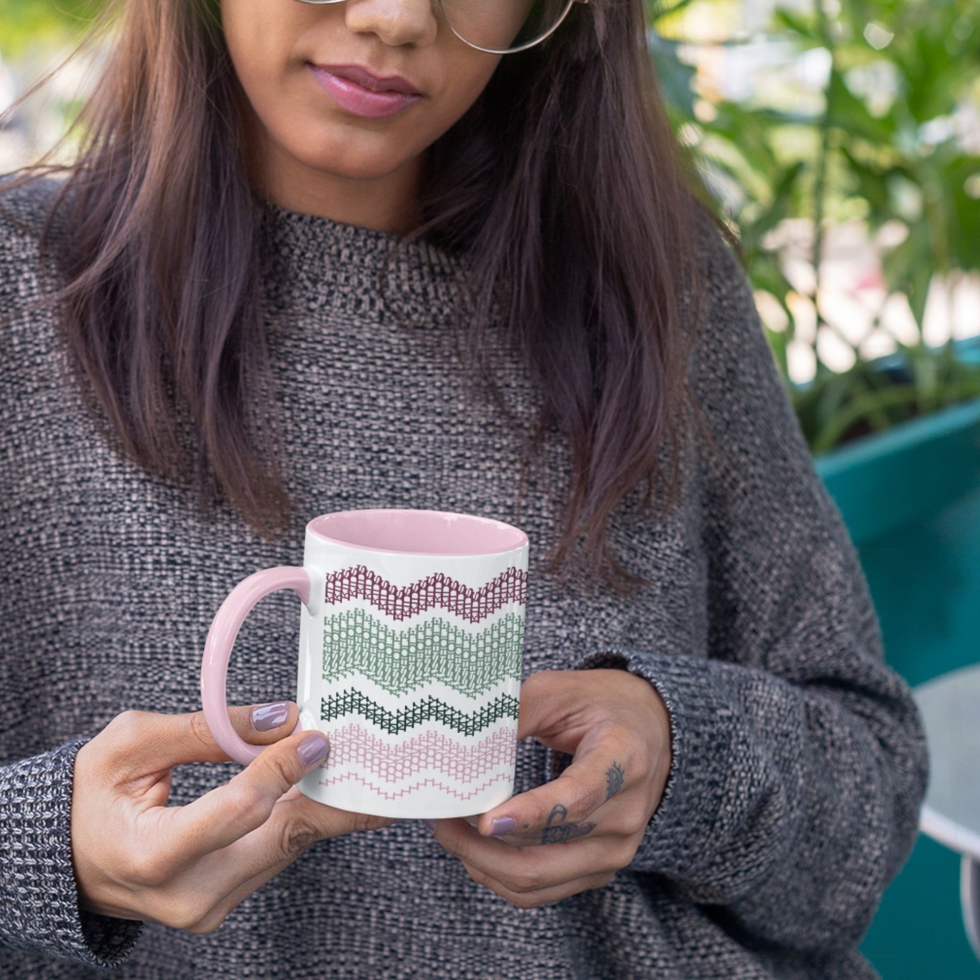 Preppy & Pink hidden message mug 11oz held in both hands outdoors with green plants in background — showing the full burgundy, sage, forest green, and pink typographic pattern