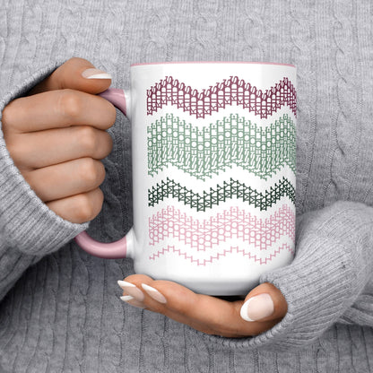 Preppy & Pink hidden message mug 15oz cradled in two hands wearing a gray cable-knit sweater — cozy lifestyle shot showing full typographic cross-stitch pattern in botanical tones