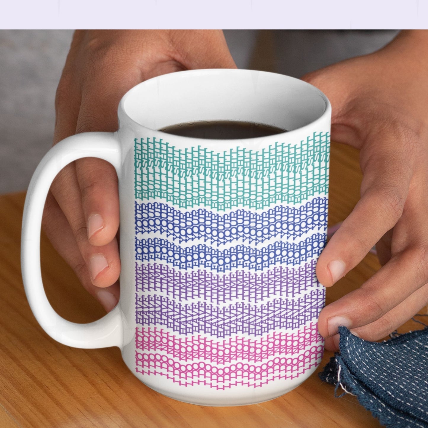 Two hands holding a 15oz bright stripe embroidery pattern ceramic mug filled with coffee on a wooden surface, showing the full teal to pink gradient "I do not have time for your bullshit" hidden design