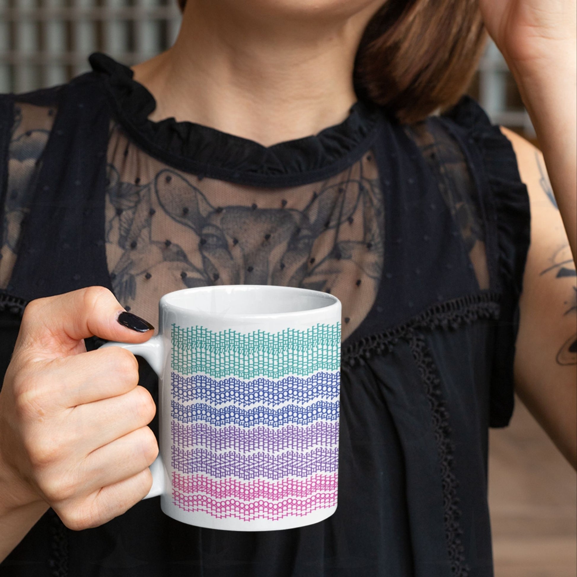 Tattooed woman in black lace top holding hidden message mug with bright embroidery stripe pattern in teal, blue, purple, and pink that spells out, "I do not have time for your bullshit"