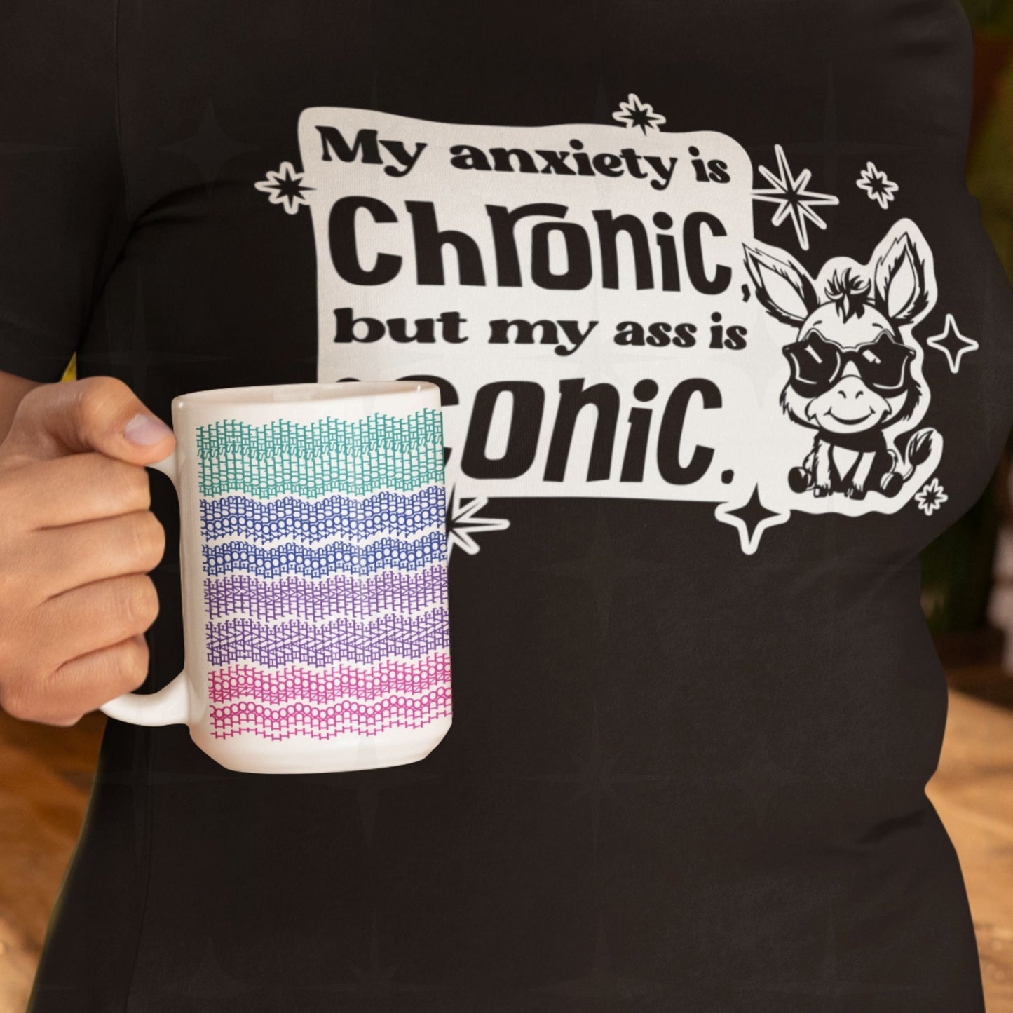 Bright embroidery pattern hidden message mug in teal, blue, purple, and pink " i do not have time for your bullshit" held in front of a dark humor slogan t-shirt, lifestyle shot