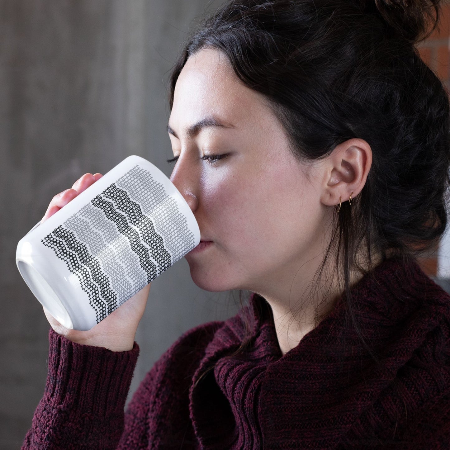 Young woman with dark hair sipping from white ceramic hidden message mug with gray and black embroidery stripe pattern, spelling, " i do not have for your bullshit"