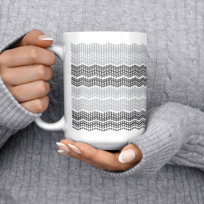 White ceramic hidden message mug with dense embroidery-style gray stripe pattern held in two hands against a gray cable-knit sweater