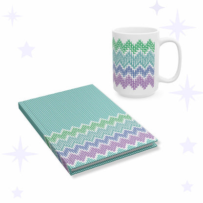 White ceramic mug and teal hardcover journal printed with a cross stitch chevron pattern spelling what the actual fuck in green, teal, blue, and violet.