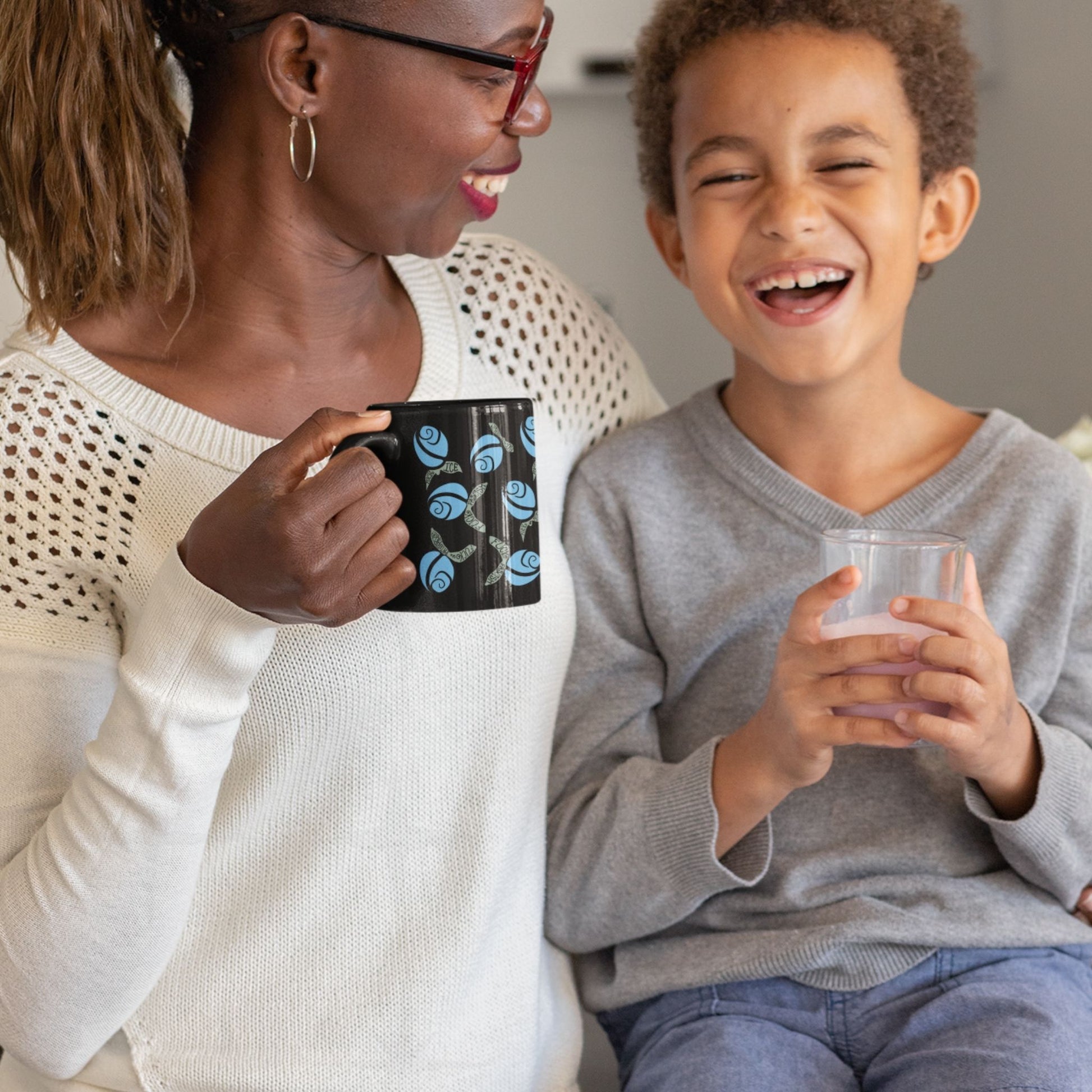 Woman laughing with child while holding blue floral hidden message protest mug on black ceramic, cornflower blue rosebuds with subversive lettered leaves