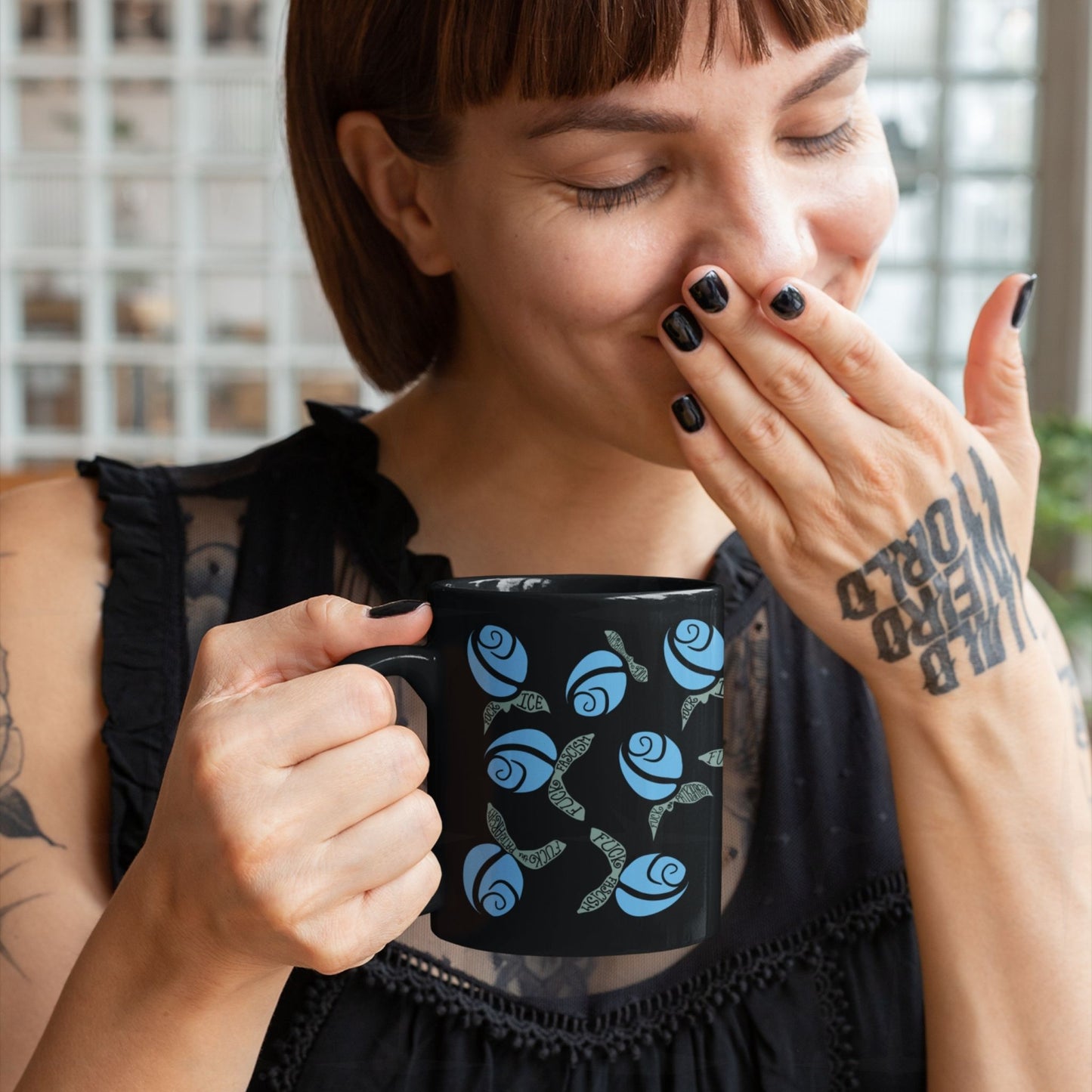 Heavily tattooed woman laughing with hand over mouth holding blue hidden message protest mug, cornflower blue rosebuds with subversive sage green lettered leaves