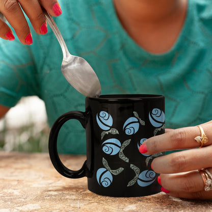 Close-up of hands with pink nails and gold rings stirring blue hidden message protest mug with a spoon, hand-lettered leaves reading Fuck ICE and Fuck Fascism visible
