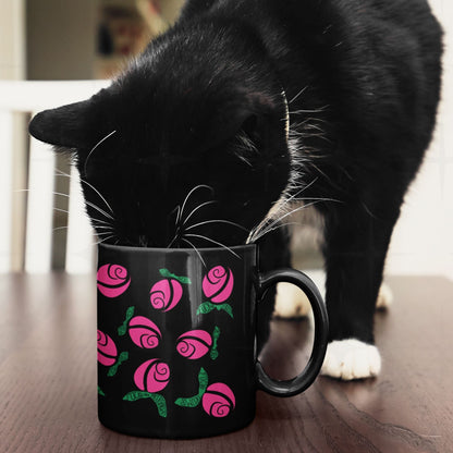 Black and white cat nosing into hot pink hidden message protest mug on wooden surface, graphic rose pattern with green hand-lettered leaves on black ceramic