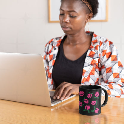 Woman working at laptop with hot pink hidden message protest mug on wooden desk beside her, graphic rosebuds with green hand-lettered leaves on black ceramic