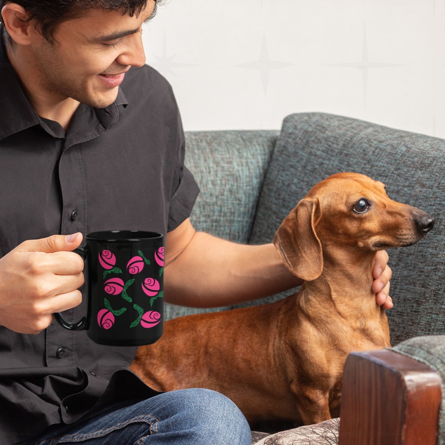 Smiling man holding hot pink hidden message protest mug while petting a dachshund on a sofa, graphic rose pattern with green hand-lettered leaves on black ceramic