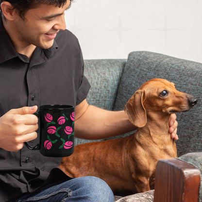 Smiling man holding hot pink hidden message protest mug while petting a dachshund on a sofa, graphic rose pattern with green hand-lettered leaves on black ceramic