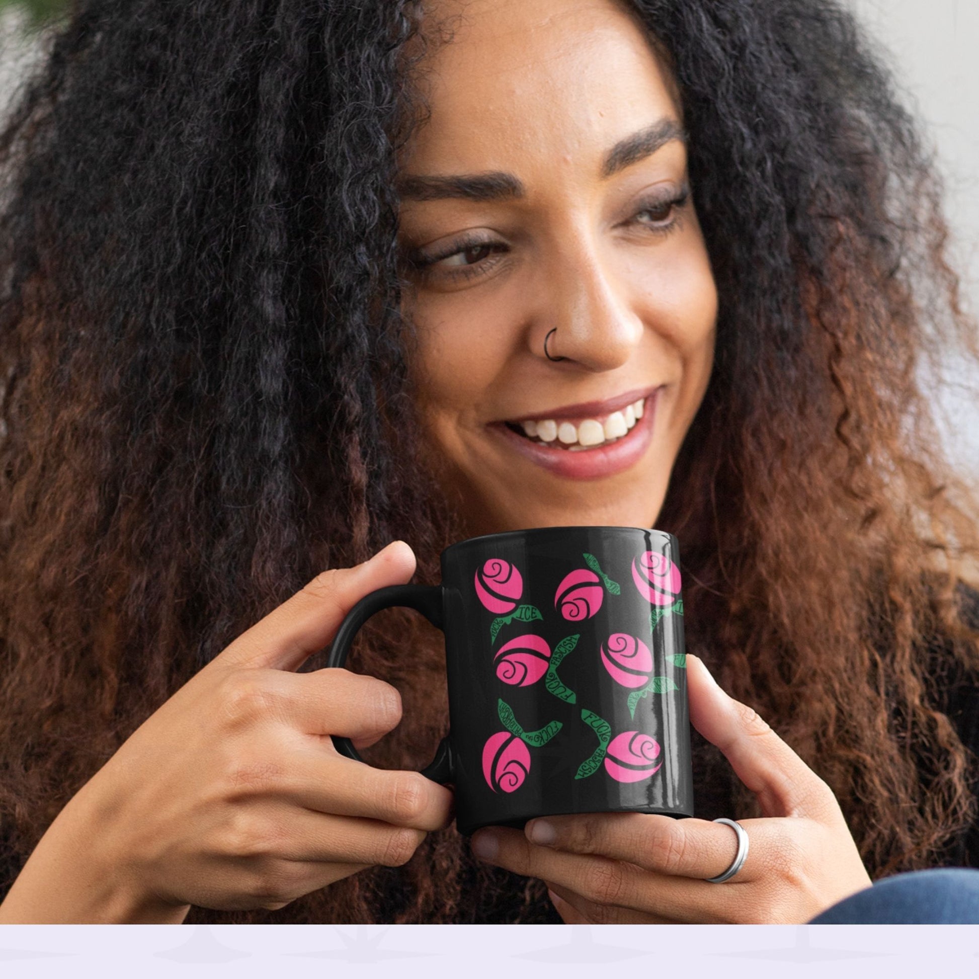 Smiling woman with curly hair holding hot pink hidden message political mug in both hands, floral protest design with green hand-lettered leaves on black ceramic