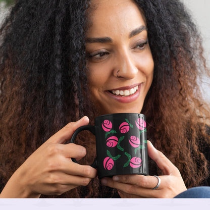Smiling woman with curly hair holding hot pink hidden message political mug in both hands, floral protest design with green hand-lettered leaves on black ceramic