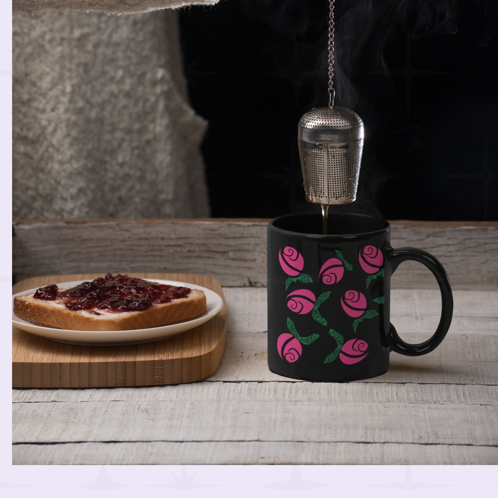 Hot pink hidden message political mug on rustic wooden table with a tea infuser being lowered in and a plate of jam toast alongside, floral protest design on black ceramic