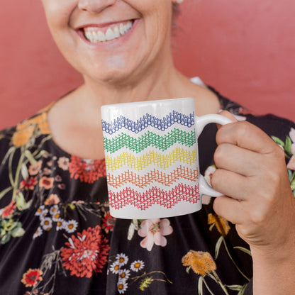 Smiling woman in black floral blouse holding rainbow stripes hidden profanity chevron mug against pink background