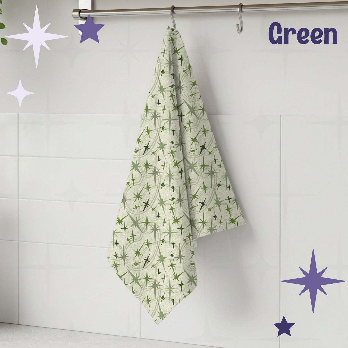 Sage green atomic starburst mid century modern tea towel hanging from a chrome hook against white subway tile, showing full pattern of olive and soft green starburst motifs on a warm cream cotton twill background