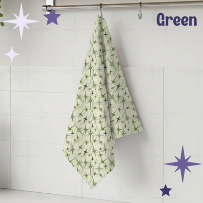 Sage green atomic starburst mid century modern tea towel hanging from a chrome hook against white subway tile, showing full pattern of olive and soft green starburst motifs on a warm cream cotton twill background