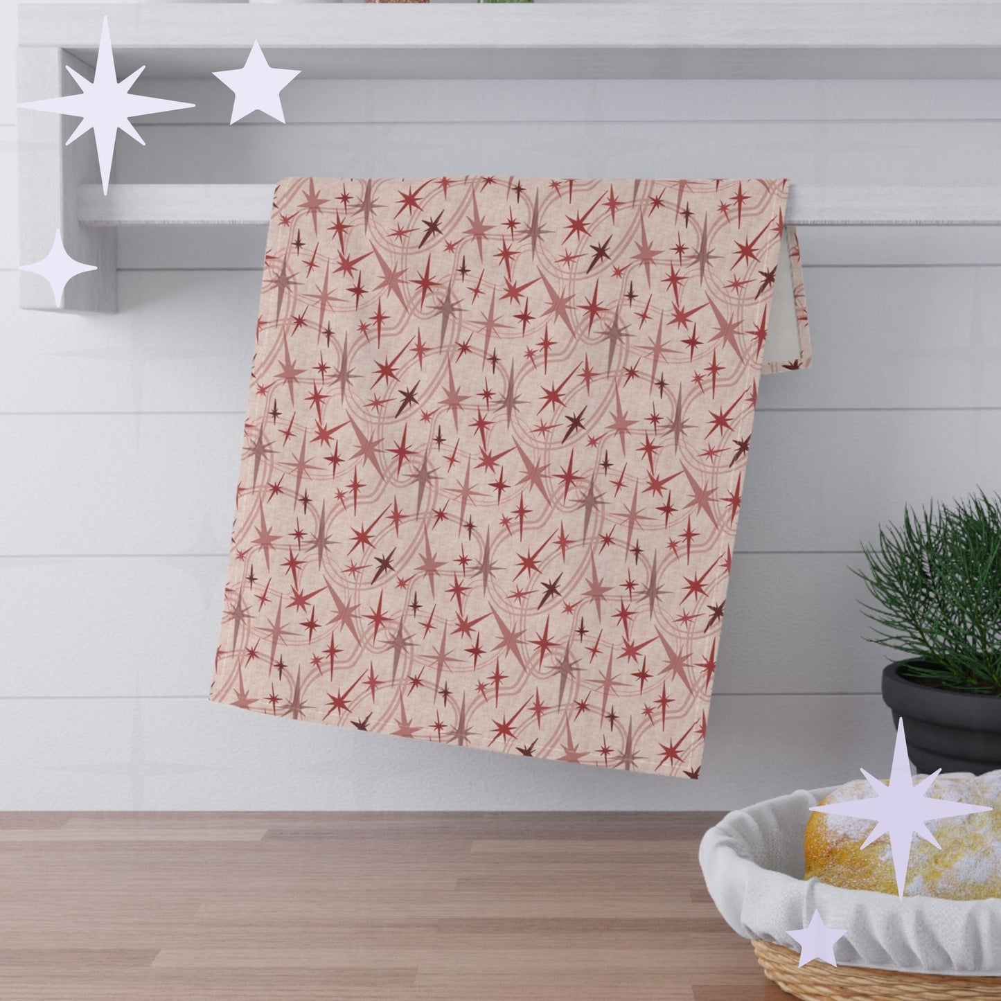 Dusty rose mid century modern tea towel with atomic starburst pattern hanging across white towel rack against white subway tile kitchen wall