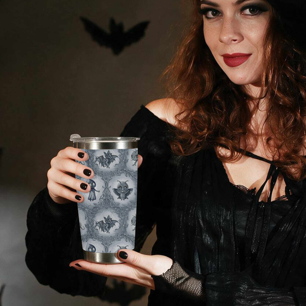 Woman in a black hat and dress holding the cryptid tumbler with paper bats on the wall behind her