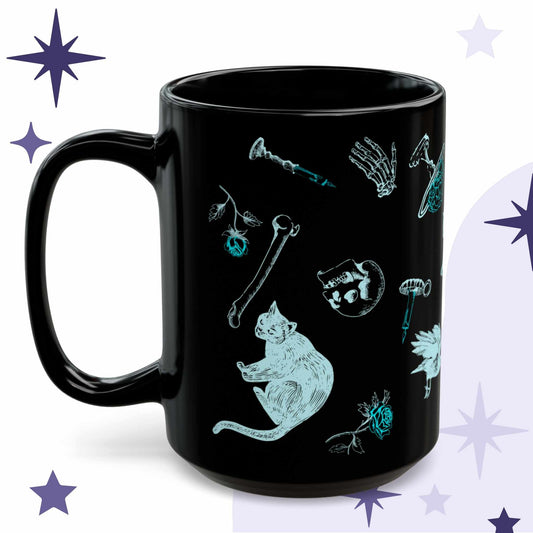 Neon goth coffee mug in black ceramic with cyan Victorian engraving of a black cat, loose bones, a skull, and roses
