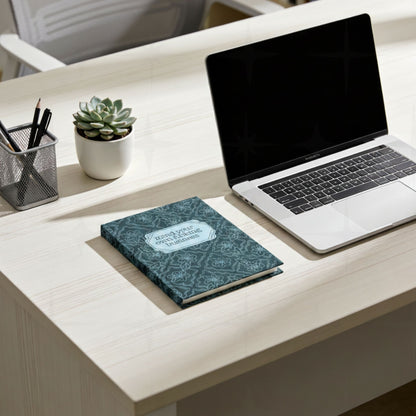Profanity floral journal on white desk next to laptop and small succulent plant showing teal botanical hardcover